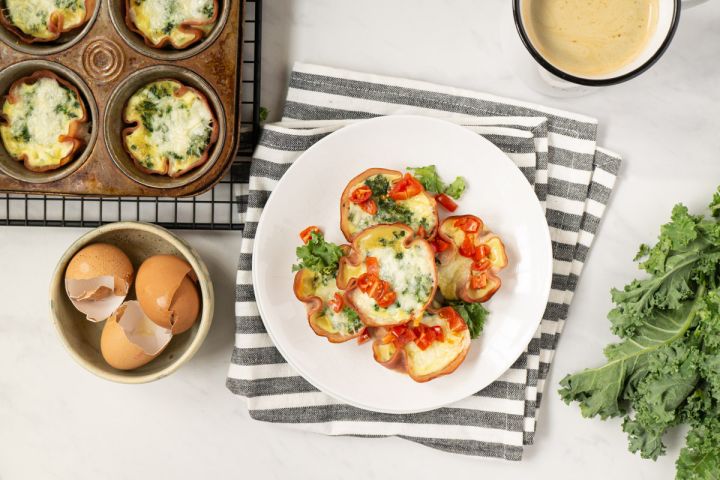 Quiche cupcakes with a ham crust and a cheese and spinach filling on a wire rack with cracked eggs on the side. 