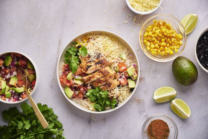 Rice bowl with cooked chicken, black beans, corn, pico de gallo, avocado, and cheese.
