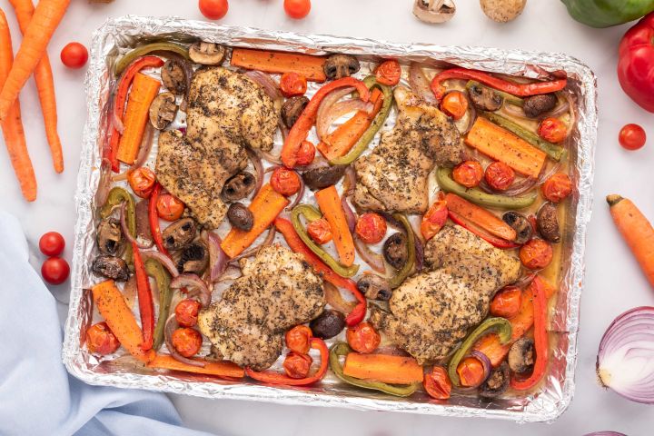 Roasted balsamic chicken thighs with vegetables on a sheet pan sprinkled with Italian seasoning.