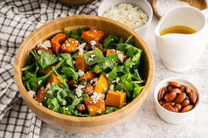 Roasted butternut squash salad with arugula, roasted squash, almonds, feta cheese, and orange vinaigrette in a wooden bowl.