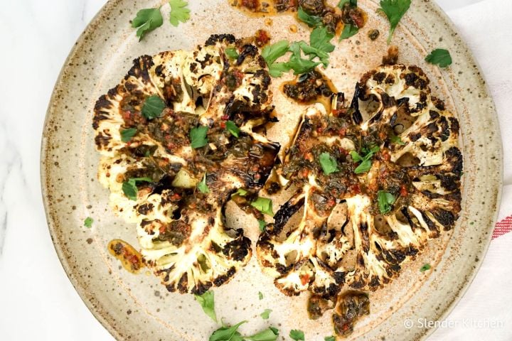 Roasted cauliflower steaks with chimichurri sauce drizzled on top.