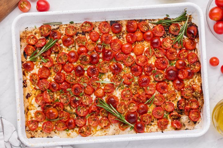 Roasted cherry tomatoes on a baking sheet with olive oil, rosemary, salt, and pepper.
