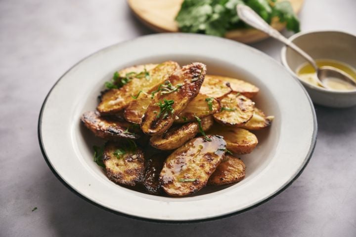 Roasted fingerling potatoes with crispy edges on a white plate with fresh herbs on the side.
