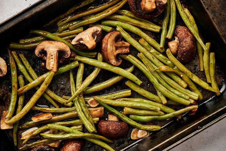 Roasted green beans and mushrooms on a baking sheet with sliced garlic and balsamic vinegar.