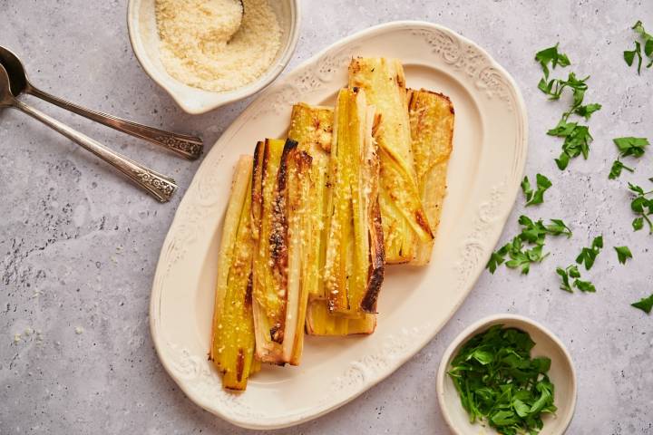 Roasted leeks with melted Parmesan cheese served on a plate with fresh thyme.