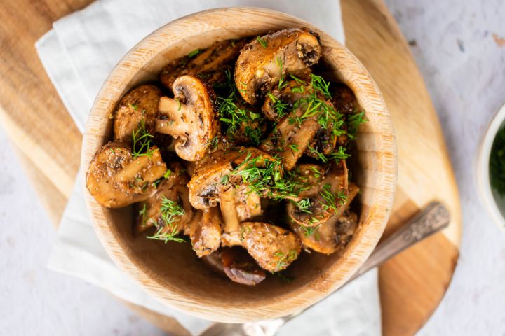 Roasted mushrooms with garlic, olive oil, and balsamic vinegar in a wooden bowl with fresh herbs. 