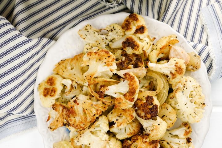 Parmesan Roasted Cauliflower with garlic cloves, parsley, and Parmesan cheese on a white plate.