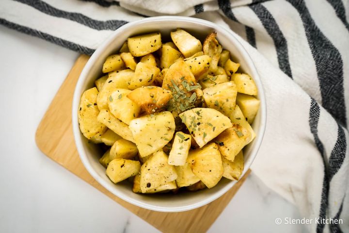 Roasted parsnips with browned edges in a bowl with dried herbs and spices.