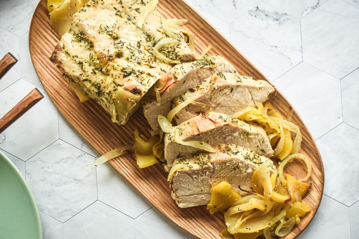 Roasted pork tenderloin and apples with sliced onions cooked and sliced on a wooden cutting board.