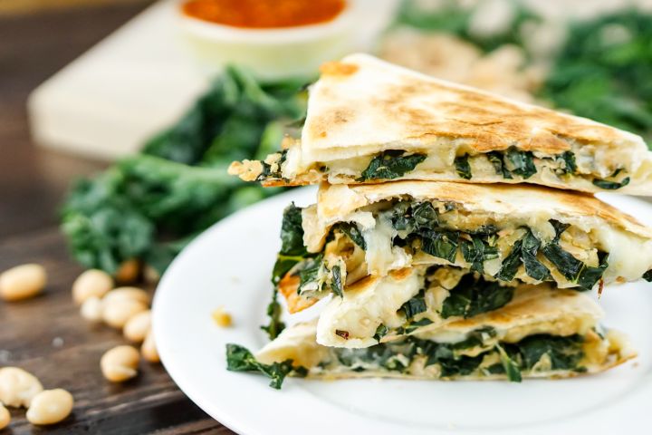 White bean and kale quesadillas stacked on top of each other with salsa and cilantro.
