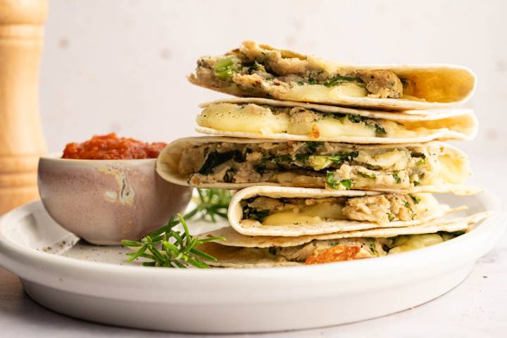 Stack of quesadillas filled with cheese and greens on a white plate, garnished with rosemary.