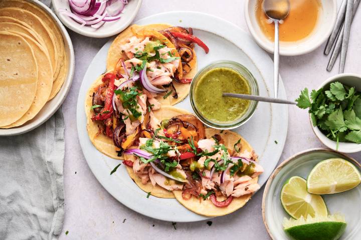 Salmon fajitas with flaked salmon, peppers, onions, cilantro, and green salsa served in corn tortillas.