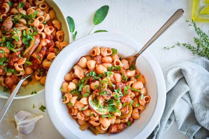 Sausage and pepper pasta with turkey sausage, bell peppers, onions, mushrooms, and tomato sauce in two bowls with garlic.