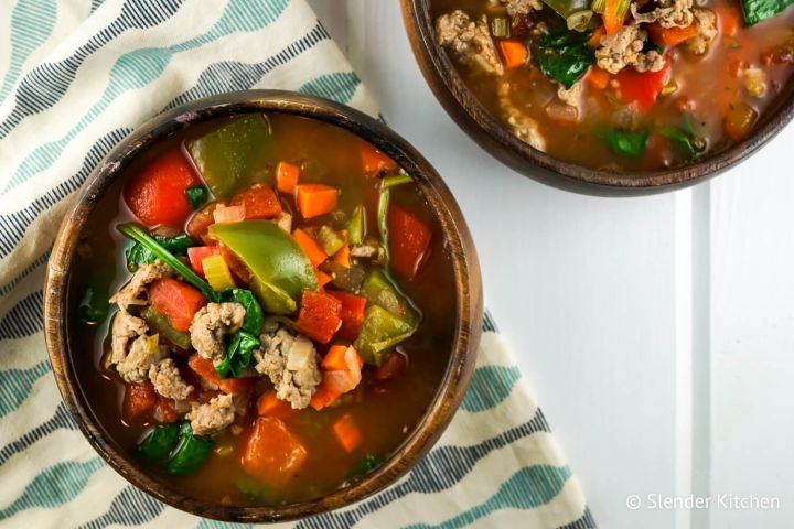 Sausage soup with peppers and spinach in a wooden bowl with carrots, celery, and tomato broth.