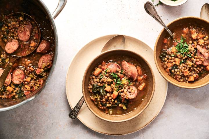 Sasuage, spinach, and lentils served in a tomato broth in two bowl and in a large soup pot.