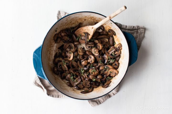 Sauteed mushrooms with garlic, butter, and thyme in a blue ceramic skillet.