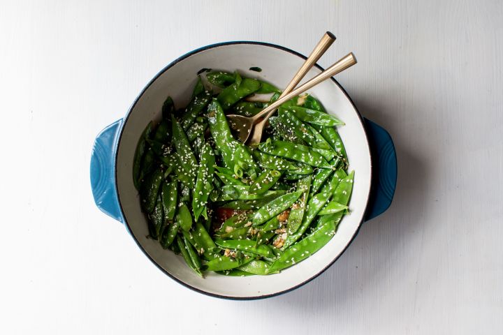 Sauteed snow peas with green onions, soy sauce, garlic, ginger, and sesame seeds with chopsticks.