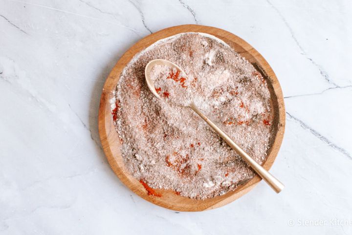 Homemade seasoned salt on a wooden plate with paprika, kosher salt, garlic powder, onion powder, and pepper.