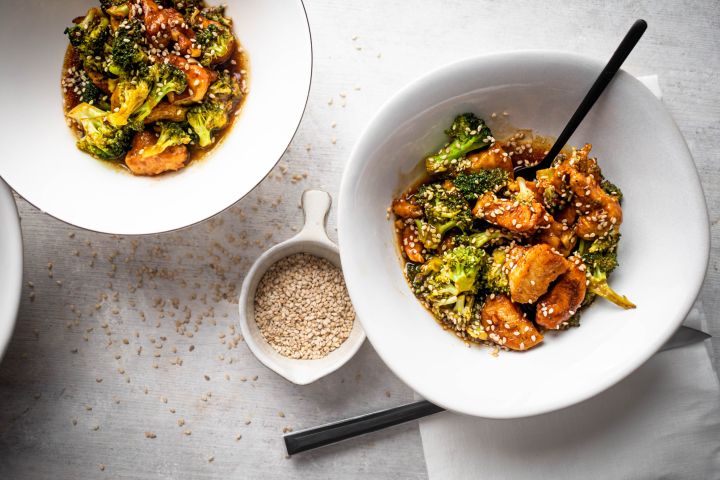 Sesame chicken with broccoli served in a bowl with sesame sauce and sesame seeds.