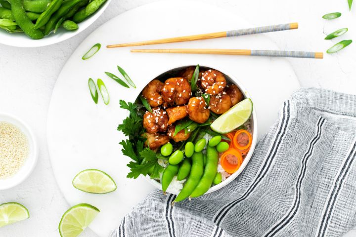 Sesame shrimp in a bowl with white rice, edamame, snow peas, and carrots.
