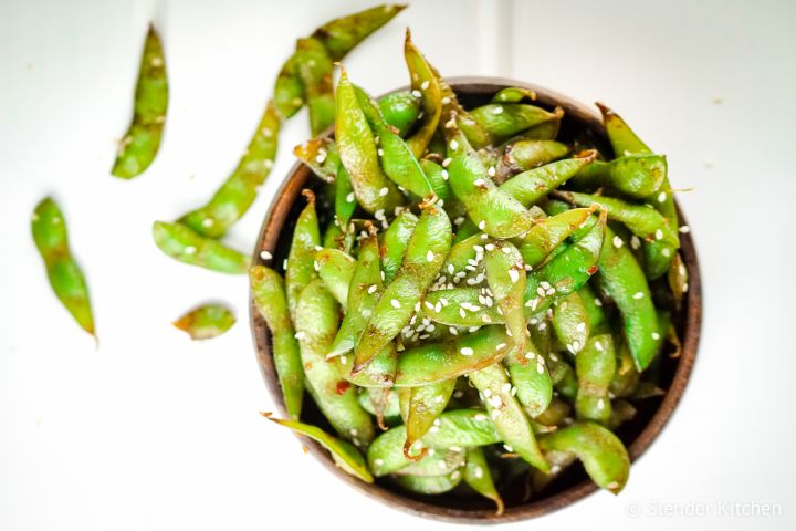 Stir fried edamame in a wooden bowl served with soy sauce and sesame seeds.