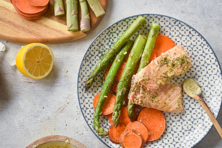 Sheet pan roasted salmon with sweet potatoes and asparagus on a plate with lemon Dijon sauce.