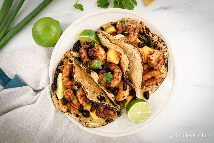 Shrimp tacos served with mango salsa served in corn tortillas with fresh lime wedges. 