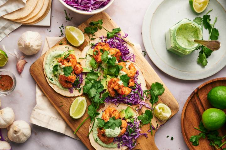Shrimp tacos served on corn tortillas with avocado, cabbage, cilantro, lime wedges, and a creamy sauce. 
