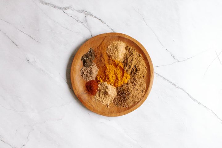 Homemade curry powder on a wooden plate with a variety of ground spices including cumin, coriander, cardamom, ginger, cinnamon, and cayenne.