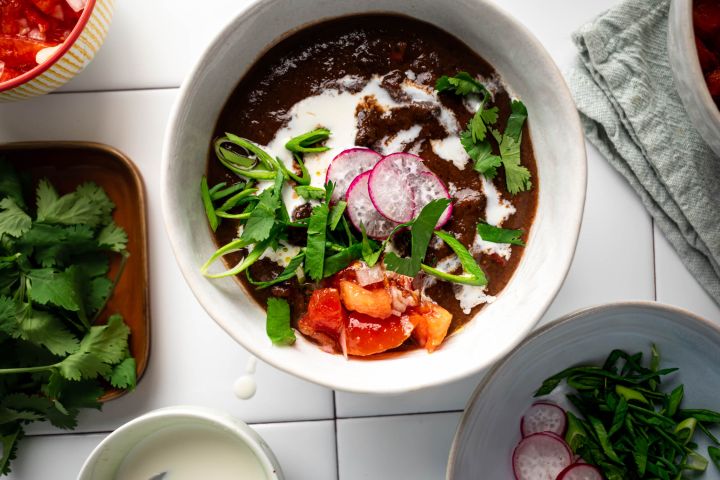 Slow cooker Black Bean Soup in a bowl with sour cream, cilantro, tomatoes, and radishes.