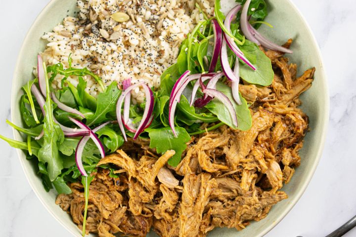 Slow Cooker Char Siu Pork in a bowl with rice, red onions, and spinach.