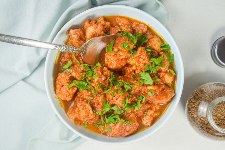 Slow cooker chicken and cauliflower tikka masala in a bowl with cilantro and spices on he side.