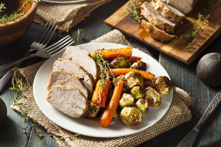 Slow Cooker Maple Pork Tenderloin sliced on a plate with carrots and Brussels sprouts.