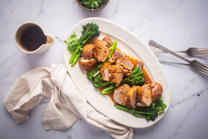 Slow cooker pork tenderloin with mustard sauce and broccolini on a white platter.