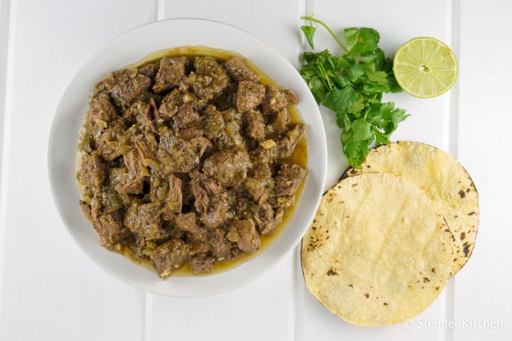 Slow cooker salsa verde beef in a bowl with fresh limes and cilantro.