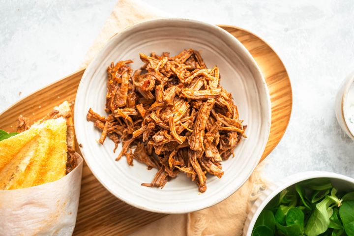 Slow cooker Italian beef in a bowl with shredded beef in a red sauce served with bread and spinach on the side.