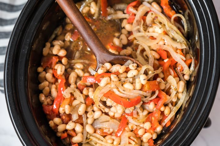 Slow Cooker Tuscan white beams with sliced red peppers, sliced onions, white beans, and spices in the crockpot.