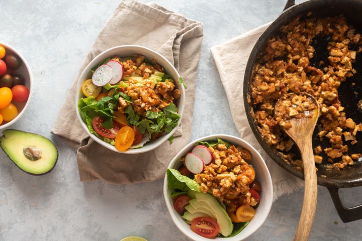 Chipotle Sofritas tofu in a skillet and served in bowls with lettuce, avocado, tomato, and cilantro.