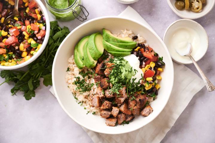 Southwest steak bowls with cooked steak, rice, black beans, cilantro, corn, pico de gallo, avocado, and sour cream.