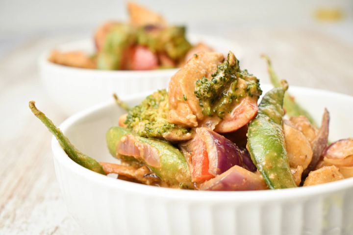 Spicy peanut chicken with vegetables in aa thick sauce in a bowl with rice.