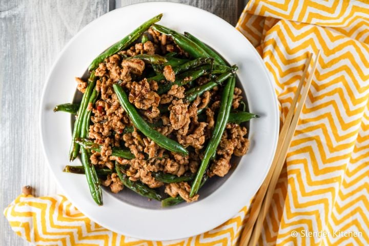 Ground turkey and green bean stir fry in a bowl with spicy sauce and chopsticks.