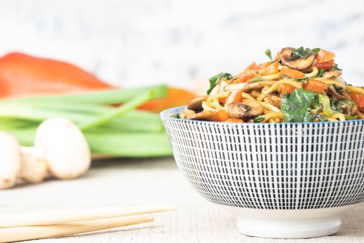 Spinach and Mushroom lo mein in a bowl with chopsticks picking up noodles.