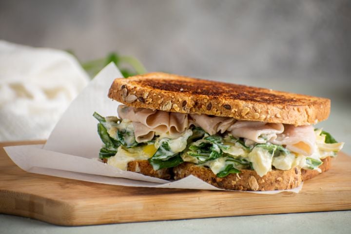 Spinach and artichoke grilled cheese sandwich with turkey breast on sliced wheat bread. 