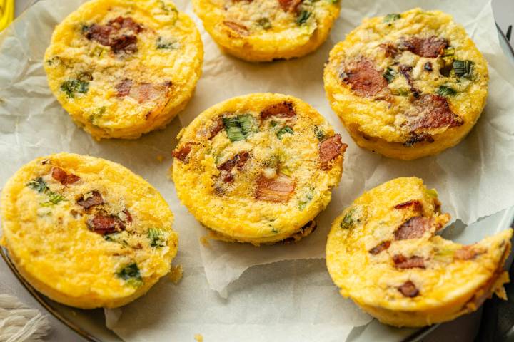 Homemade high-protein egg bites arranged on a parchment-lined plate, featuring a fluffy texture with visible bacon and green onion pieces.
