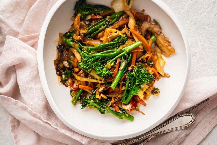 Stir fried vegetables with cabbage, mushrooms, broccoli, and carrots in stir fry sauce in a white bowl.