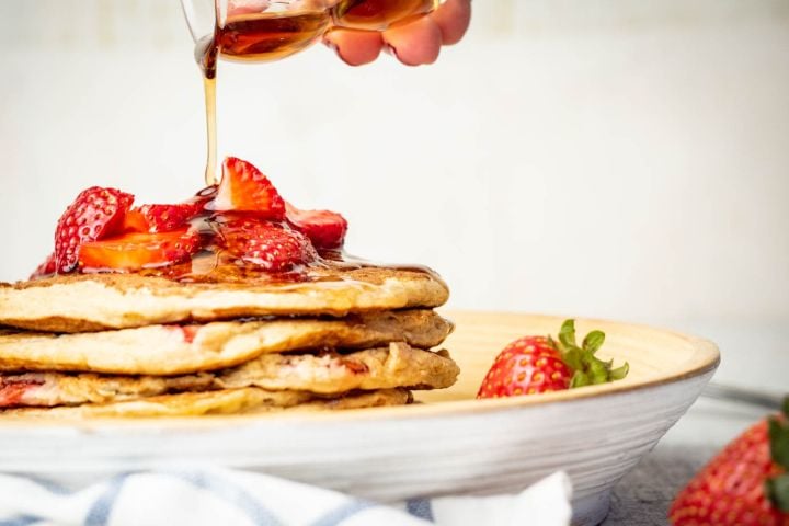 Strawberry Banana Oat Pancakes with maple syrup being poured on top.