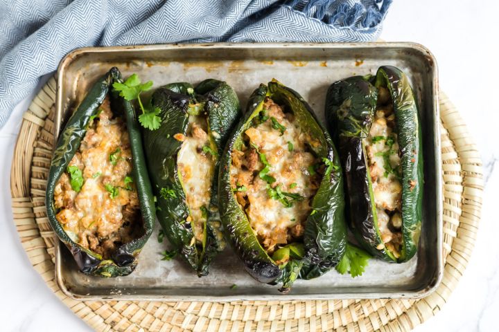 Stuffed poblano peppers with ground turkey, melted cheese, and mozzarella on a baking sheet.