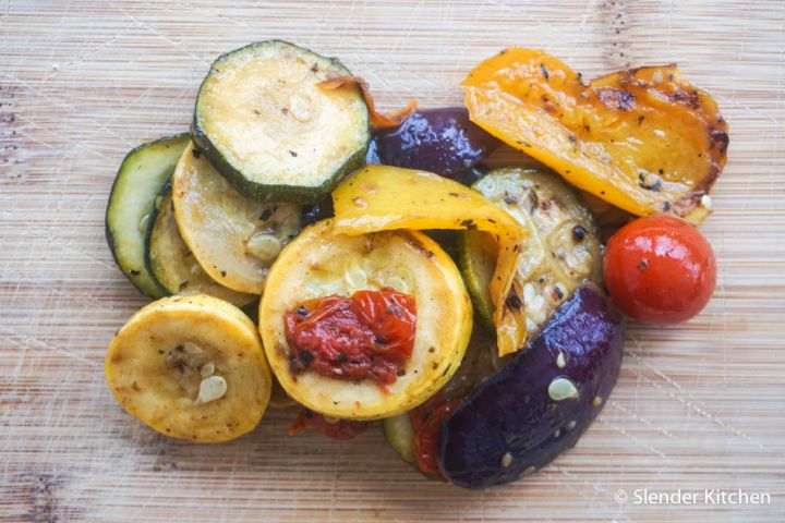 Grilled summer vegetables with zucchini, yellow squash, cherry tomatoes, red onion, and red bell peppers on a cutting board.