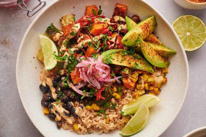 Sweet potato bowls with roasted sweet potatoes, black beans, corn, peppers, onions, zucchini, and brown rice topped with avocado, cilantro, and limes.