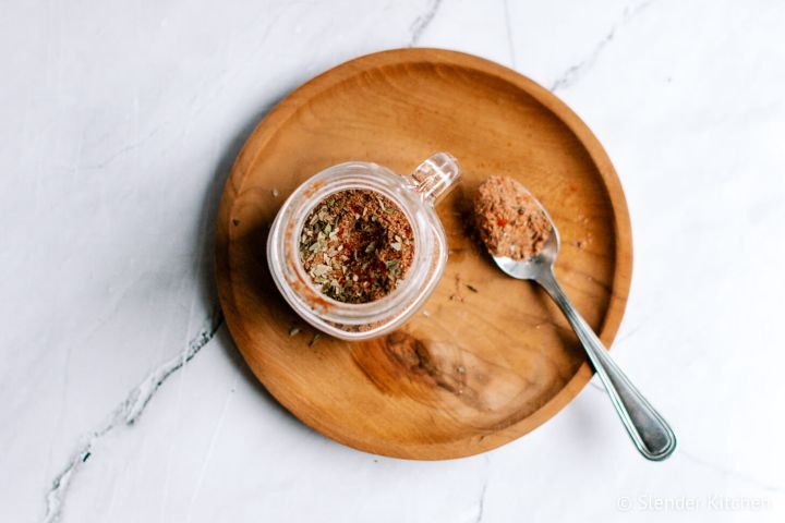 Homemade taco seasoning in a small jar with a spoon including chili powder, oregano, paprika, cumin, and other spices. 